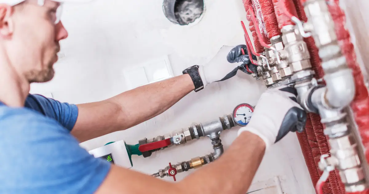 A male plumber demonstrating what is backflow testing about by inspecting water pipes at a residence.